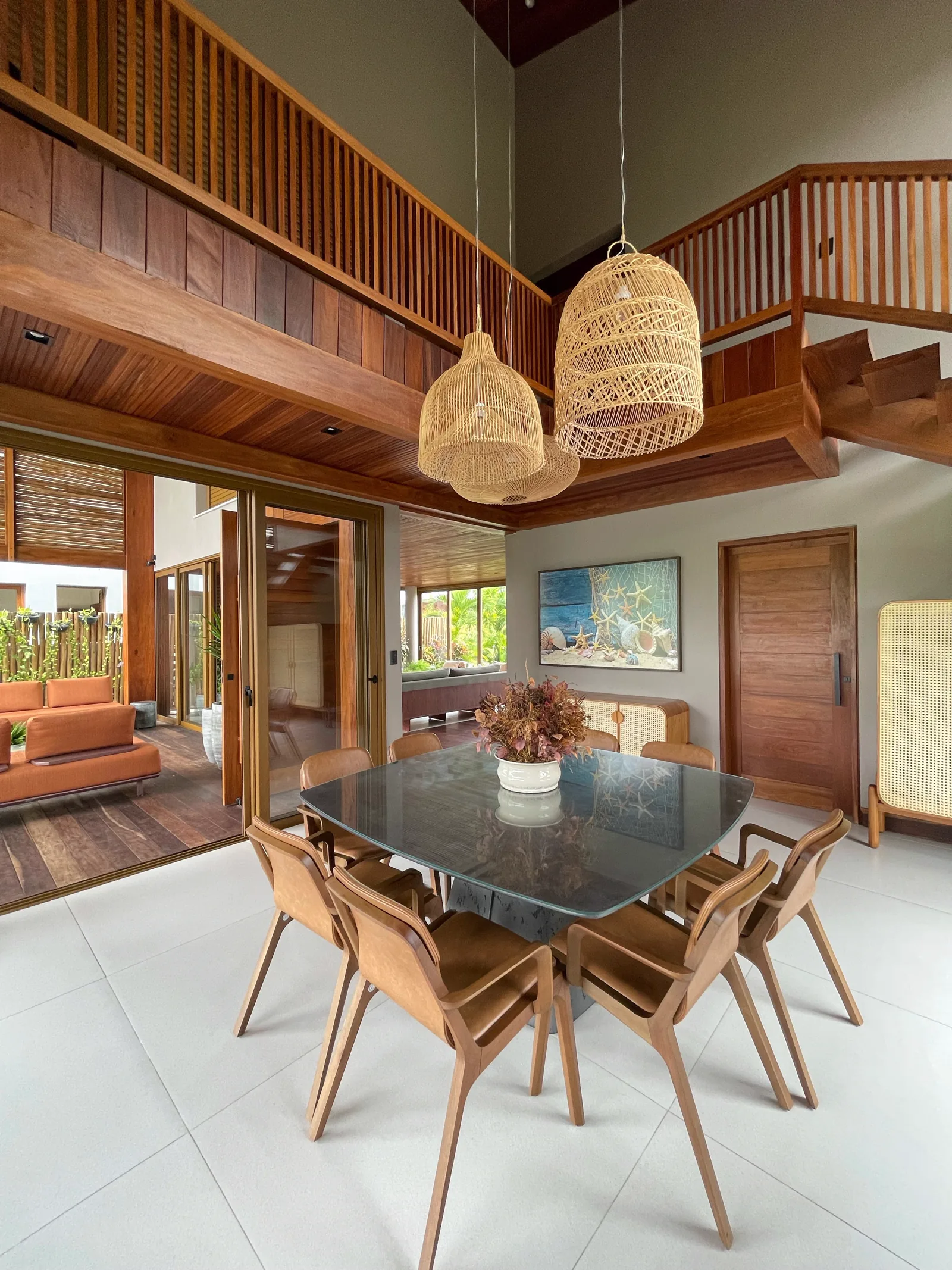 Sala de jantar com pendentes de vime, pé-direito duplo e mezanino em madeira