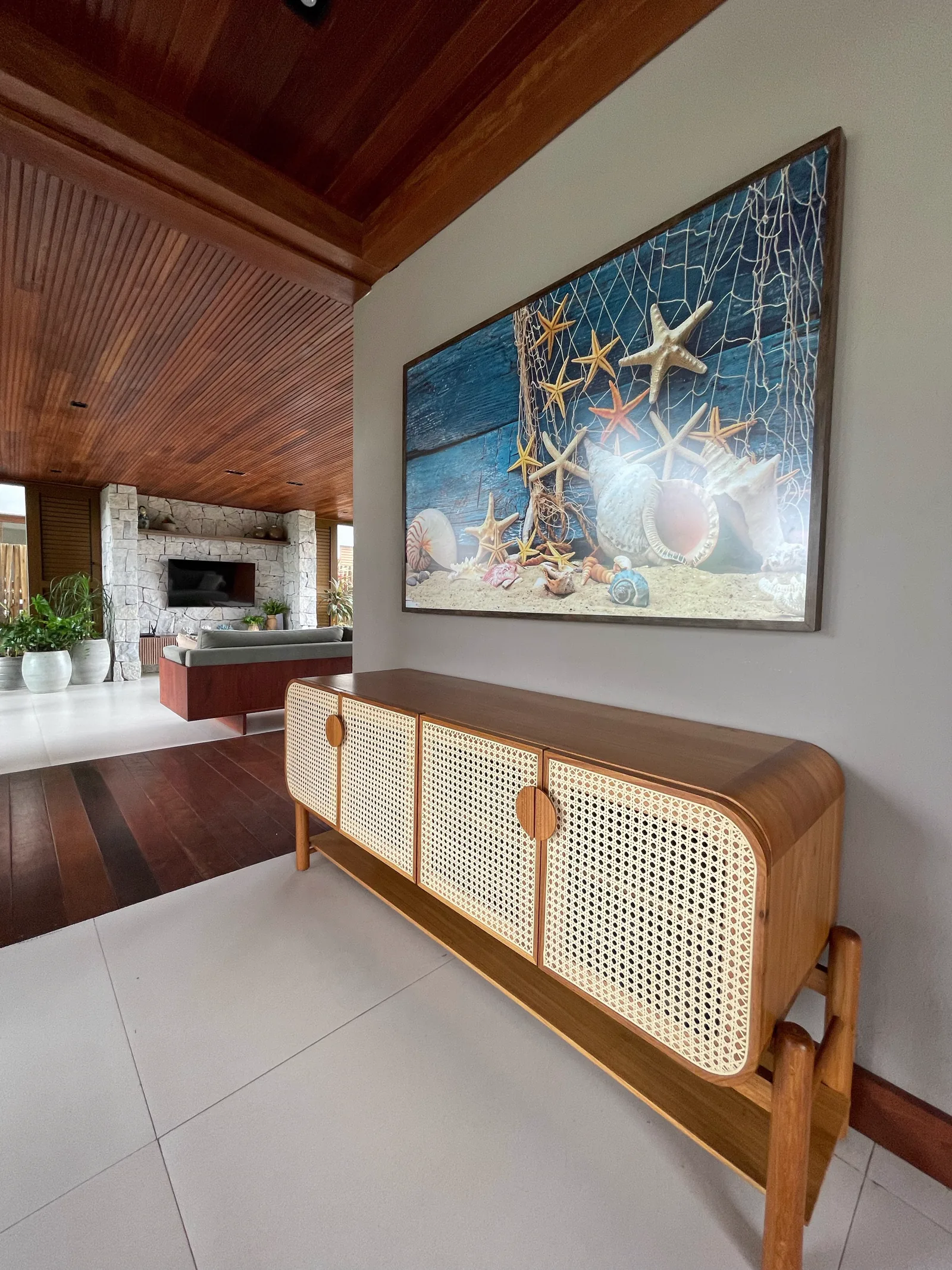 Hall com aparador de palhinha e quadro de conchas, com vista para o living