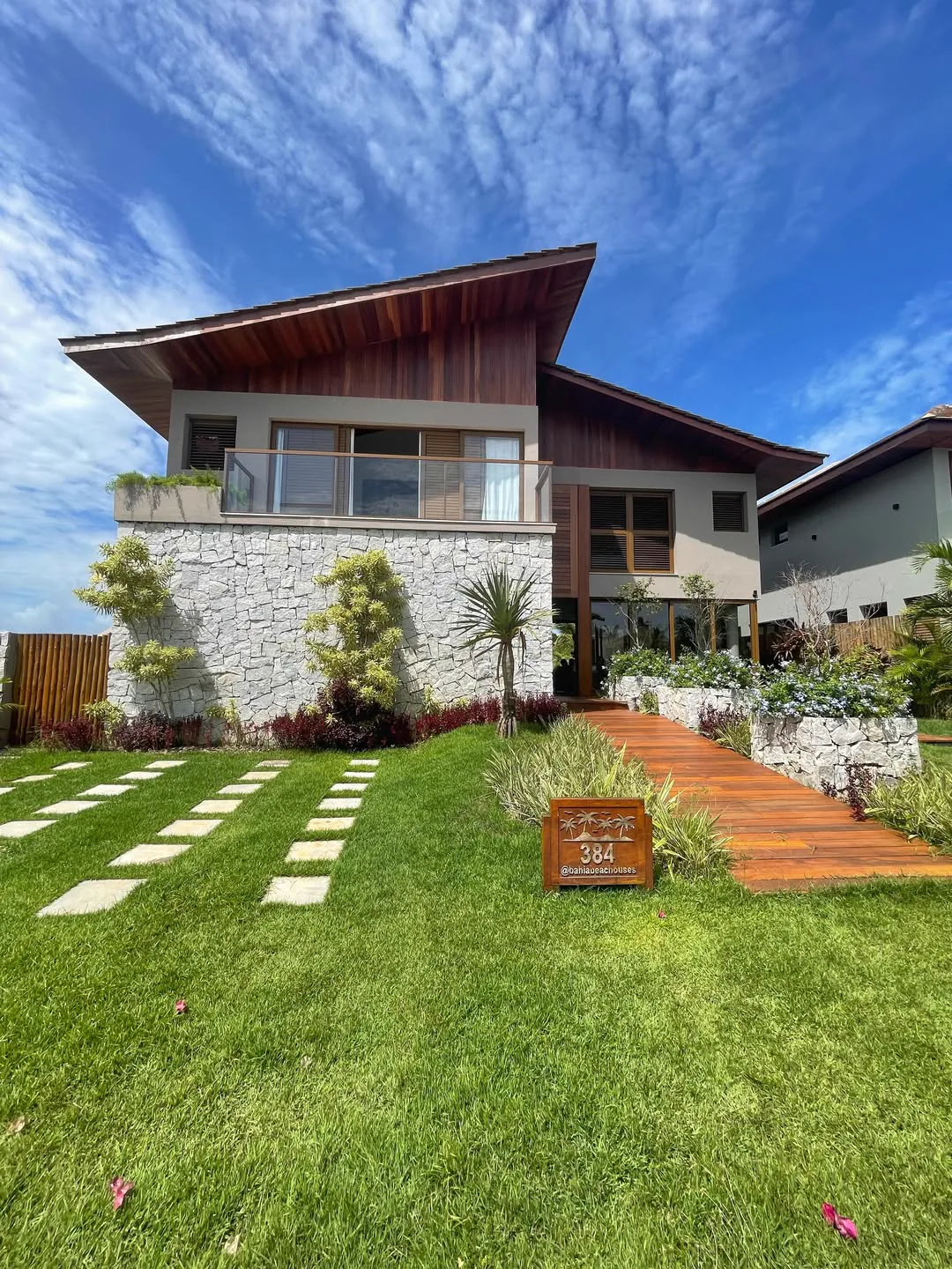 Fachada da Casa 384 com base em pedra e jardim, sob o céu da Praia do Forte