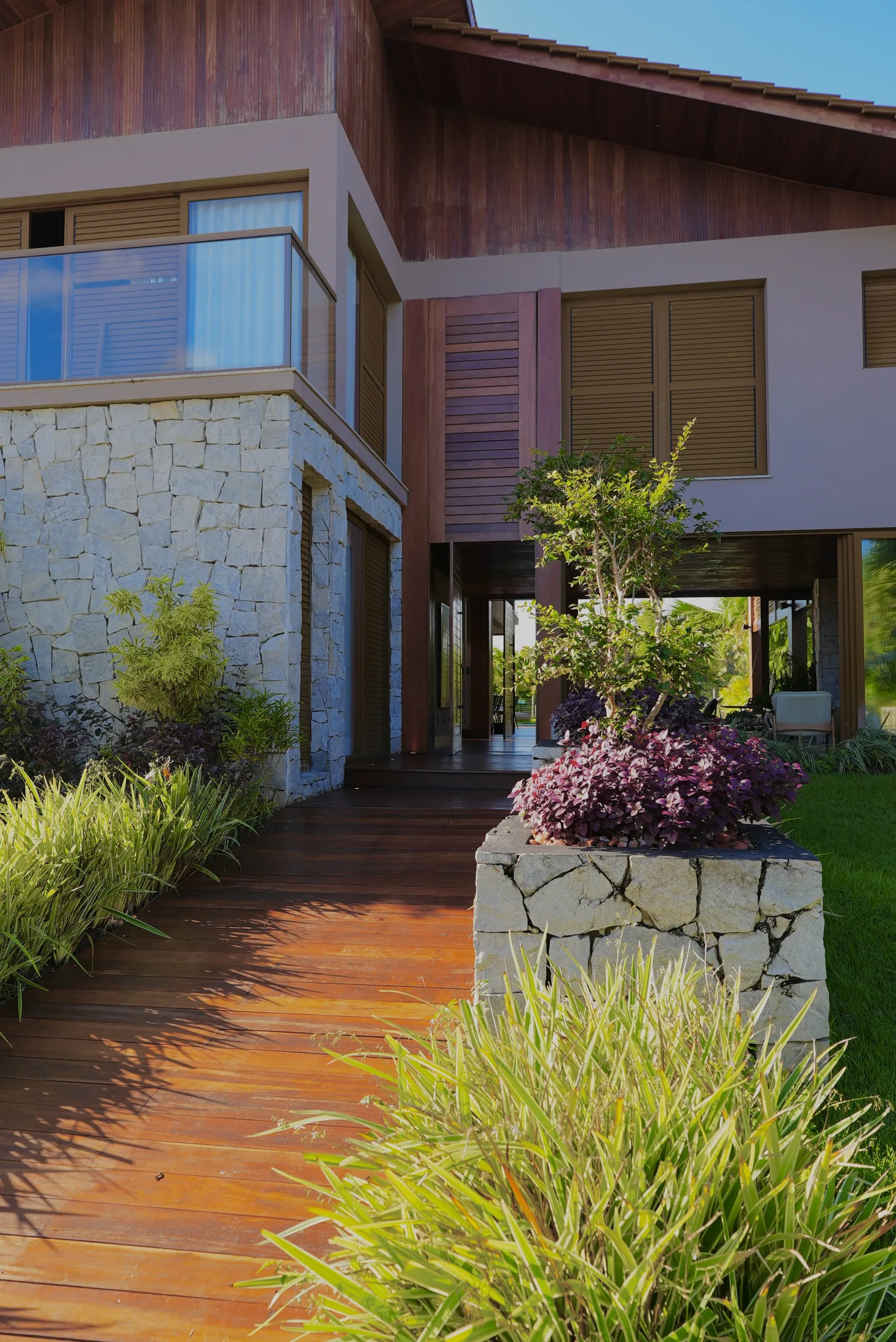 Base da casa em pedra e deck de madeira, com o jardim ao redor