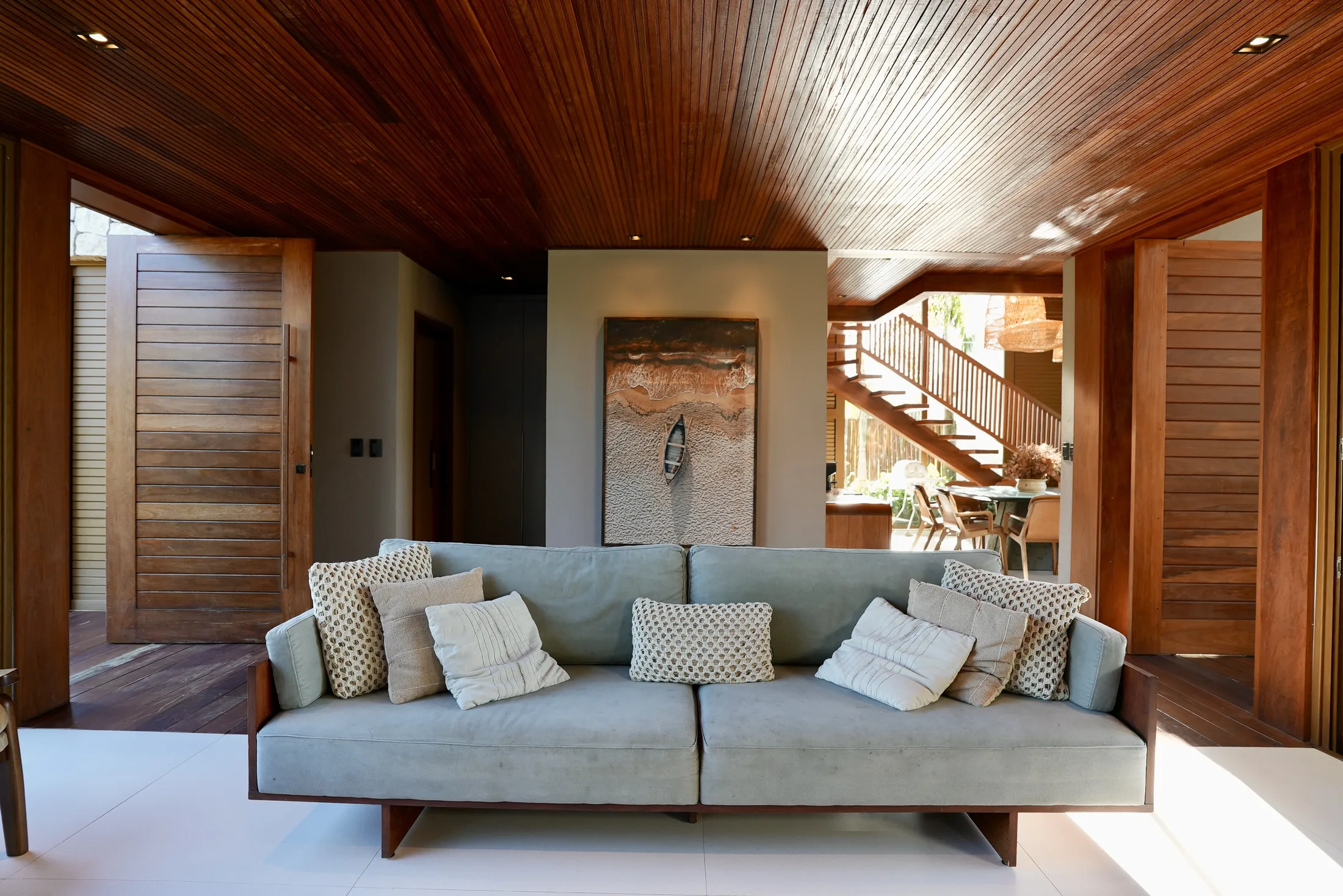 Sofá do living com quadro do mar e a escada de madeira ao fundo