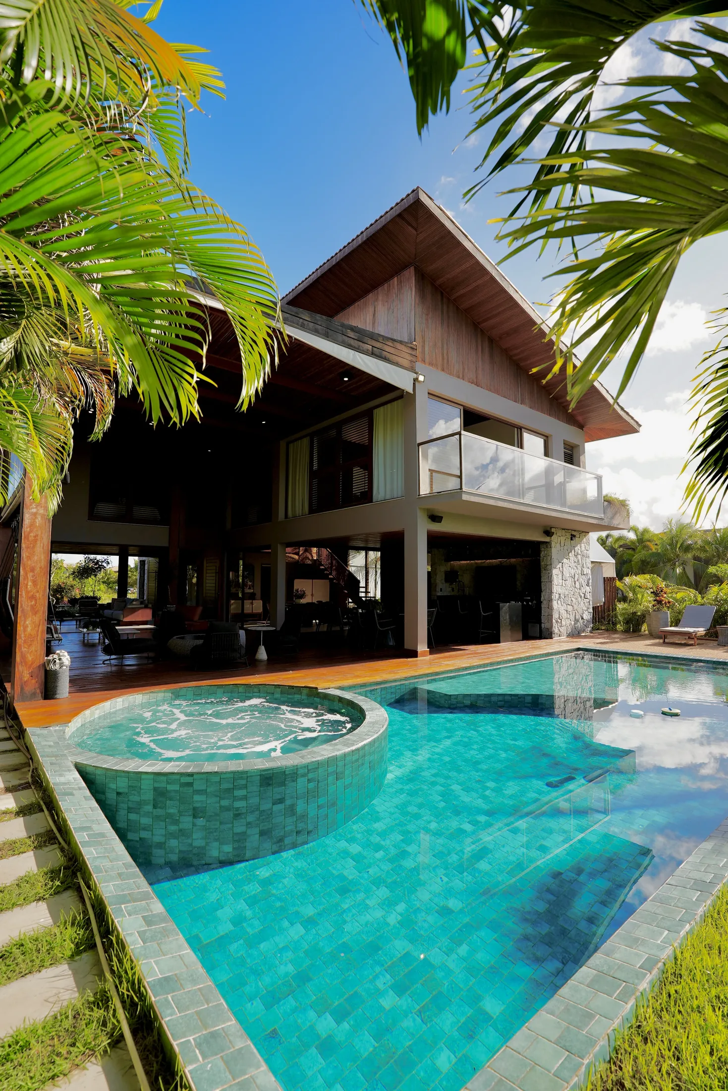 Piscina com jacuzzi e a fachada da casa entre coqueiros